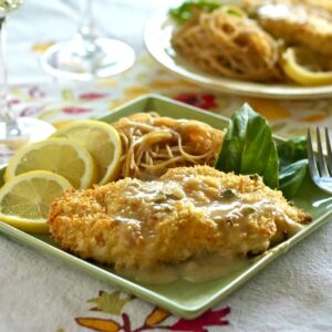 Baked Chicken Piccata on a plate with lemon slices, herbs and pasta