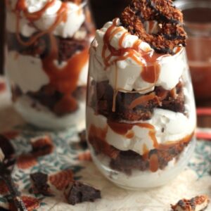 2 Samoa brownie parfaits in stemless wine glasses with cookie pieces scattered around them