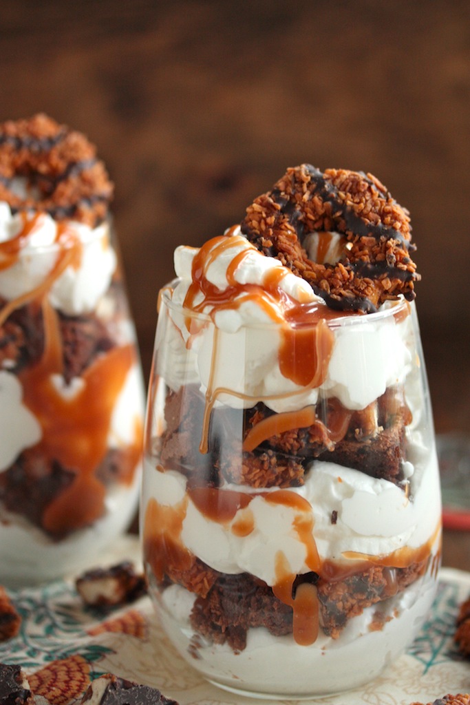 Layers of whipped cream, brownies, caramel, and Samoa cookies in stemless wine glass