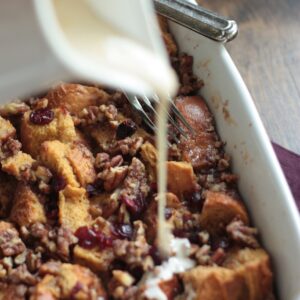 Cranberry Bread Pudding with creamy rum sauce being poured over top