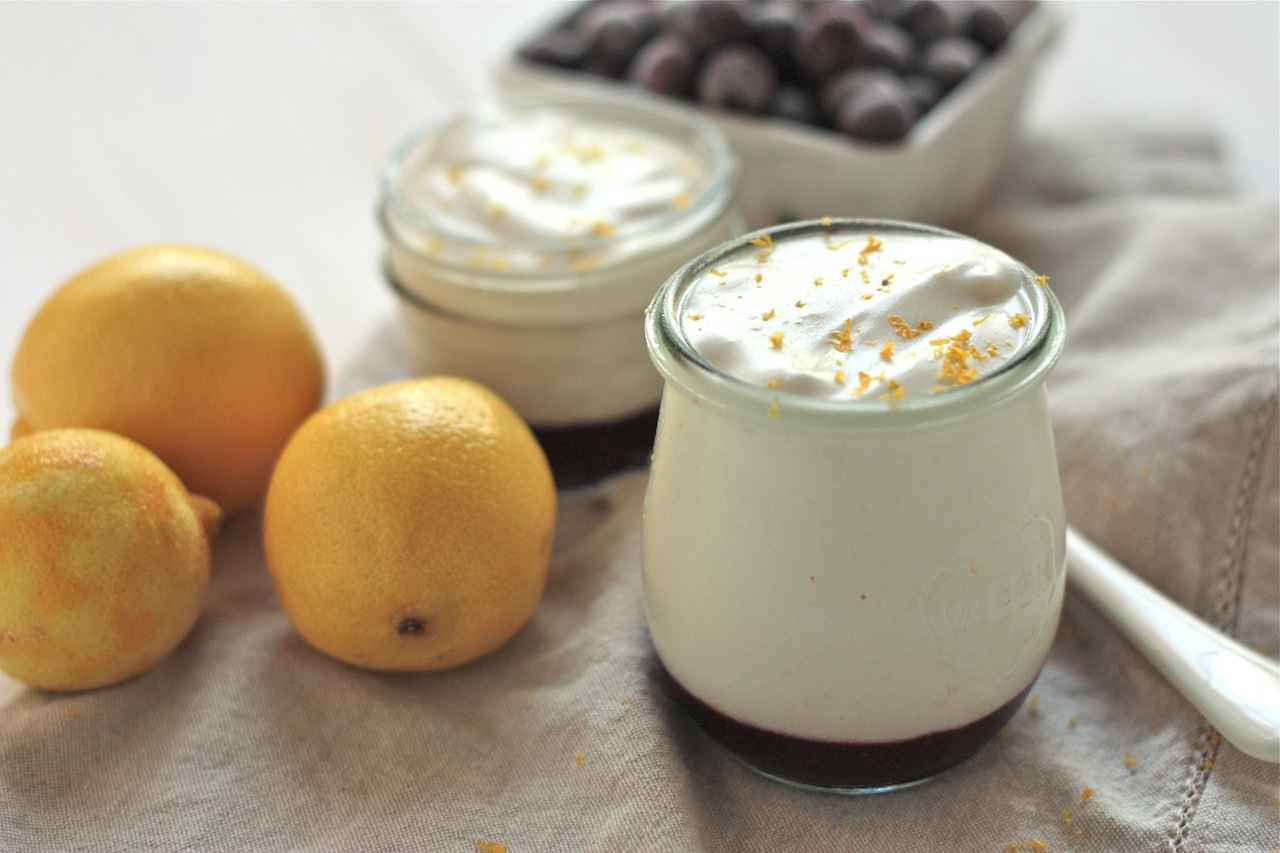 Two glass jars filled with lemon mousse with lemons and pint of blueberries in background