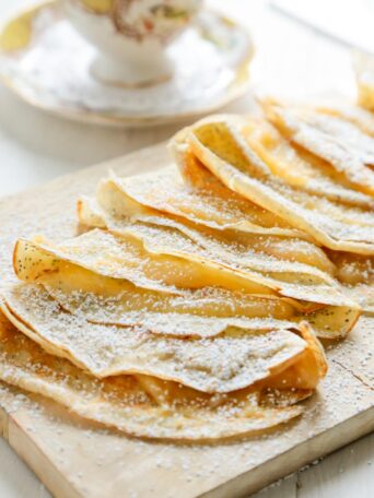 Lemon Poppyseed Crepes with Lemon Curd - on a cutting board with yellow and white tea cup