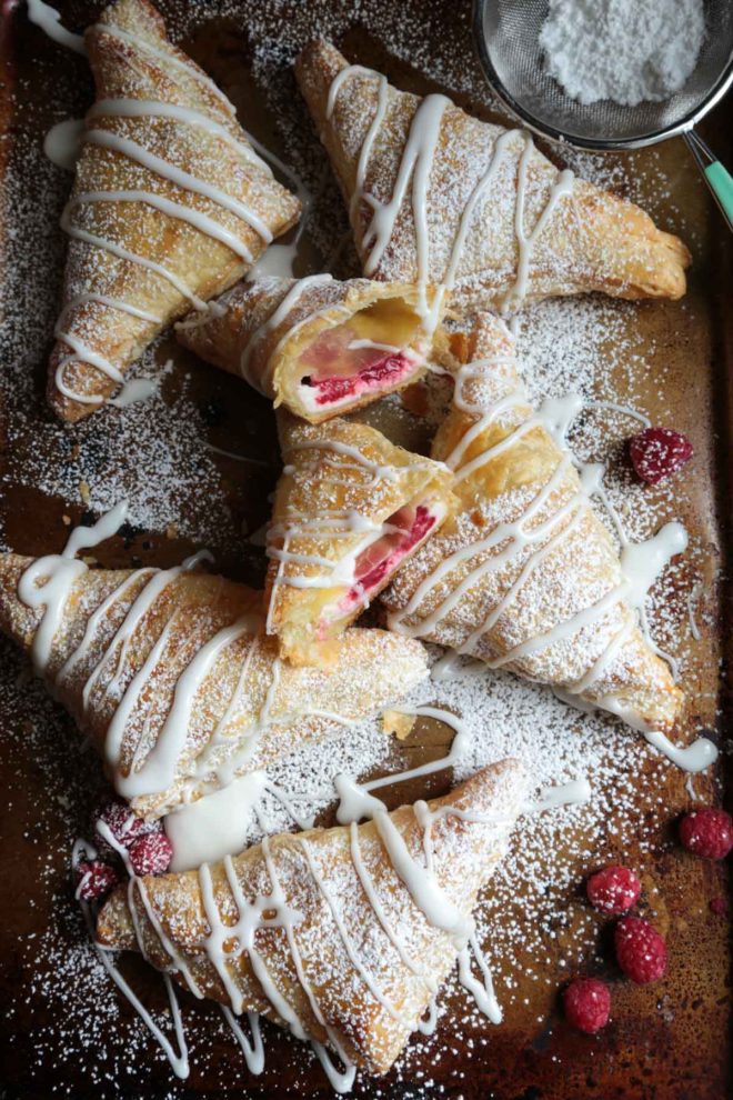 Easy Raspberry Cream Cheese Turnovers - Done in 30 minutes! on a baking sheet with scattered raspberries all around