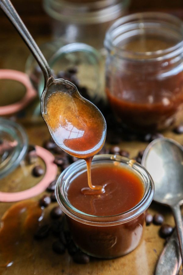 Homemade Coffee Salted Caramel Sauce dripping from a spoon into a jar with coffee beans