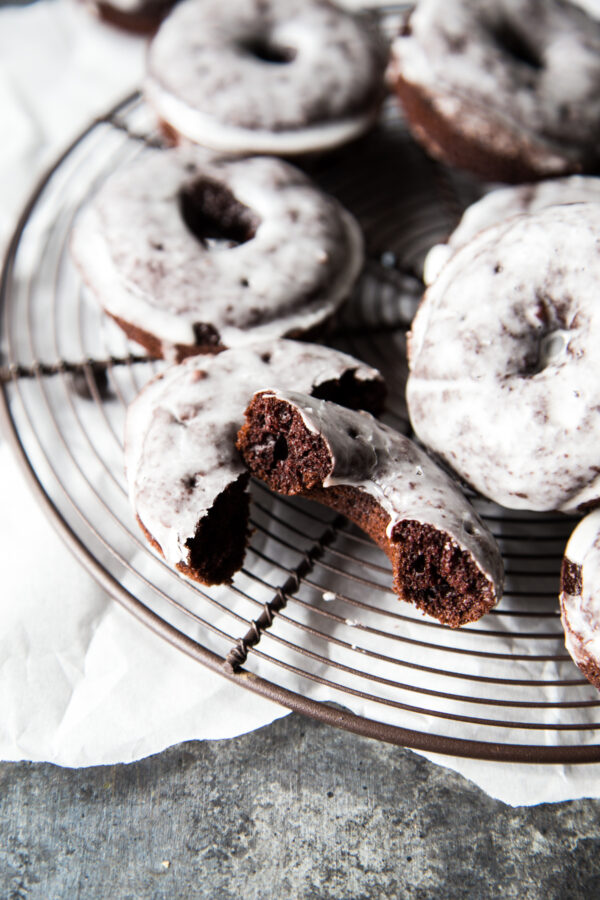 Stack of chocolate glazed cake doughnuts on a wire rack set on top of parchment paper with one cut in half.