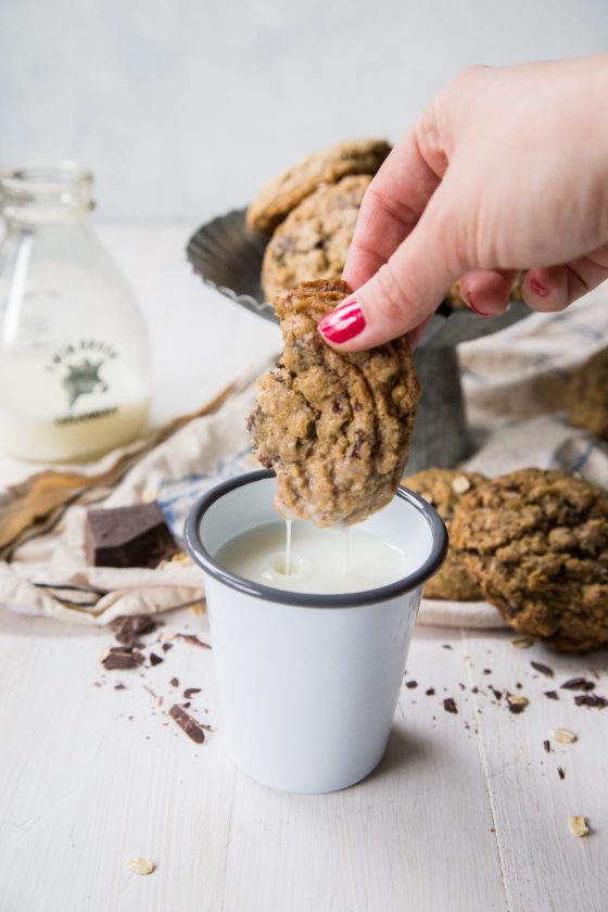 Dark Chocolate Chunk Oatmeal Coconut Cookies being dunked into a white and gray cup of milk