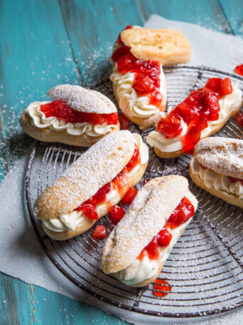 Strawberry Cheesecake Eclairs on a blue background and cooling rack
