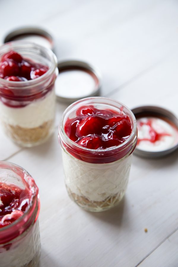 No Bake Cheesecakes In A Jar with cherries on top in mason jars with lids on white background