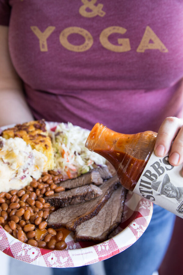 Plate of brisket, beans, coleslaw, and pouring bottle of barbecue sauce on top of meat