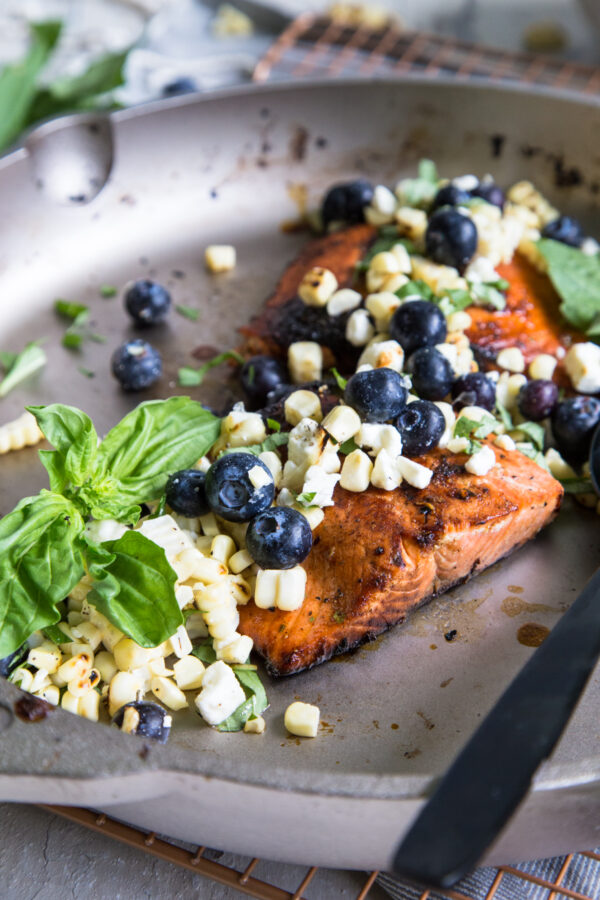Wild Salmon with Blueberry Corn Salsa in a cast iron pan with black utensils and basil leaves