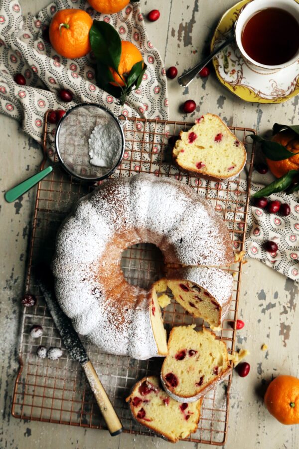 Cranberry Orange and Almond Sour Cream Bundt Cake on a copper cooling rack with oranges and cranberries