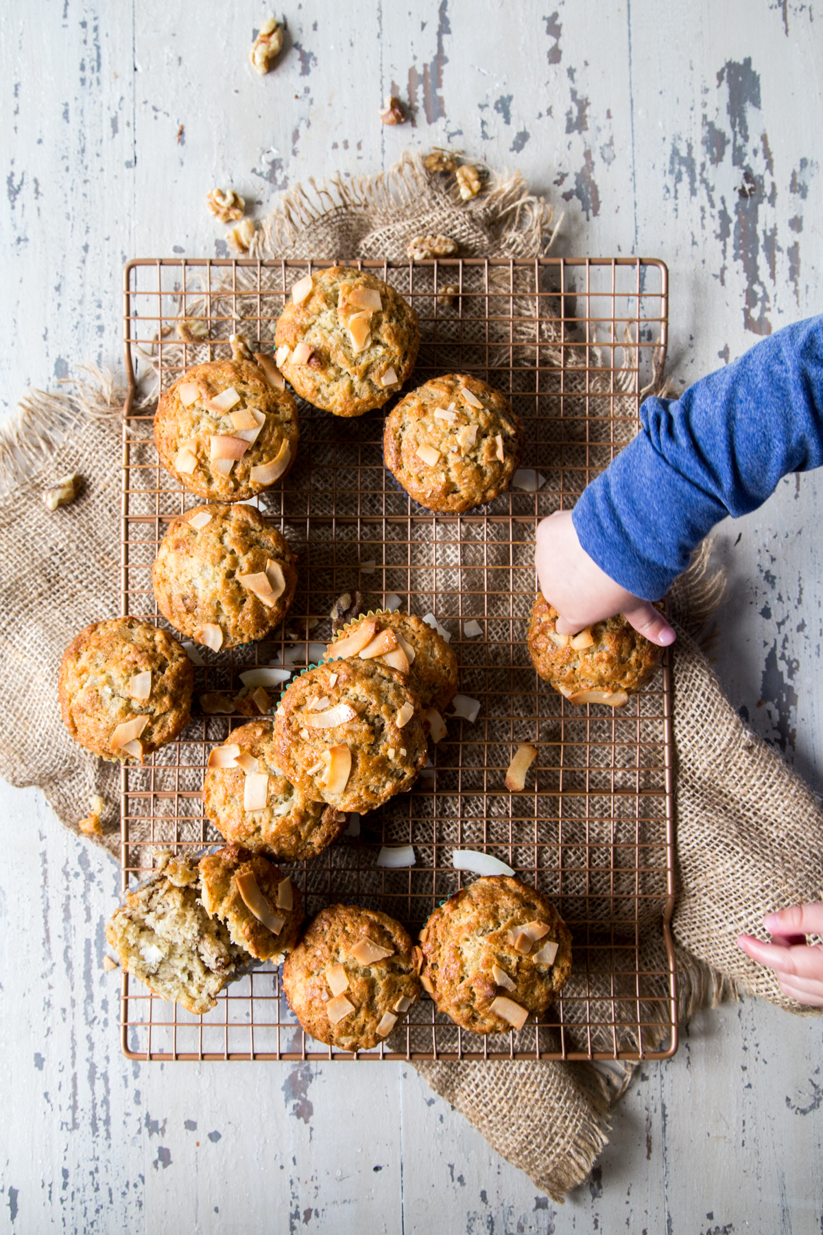 Coconut banana muffins on a copper wire rack on a distressed white background shot overhead