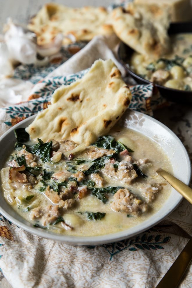 sausage kale and gnocchi soup in a white bowl with naan bread for dipping