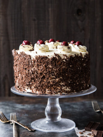 black forest cake on a glass cake stand with dark wood background
