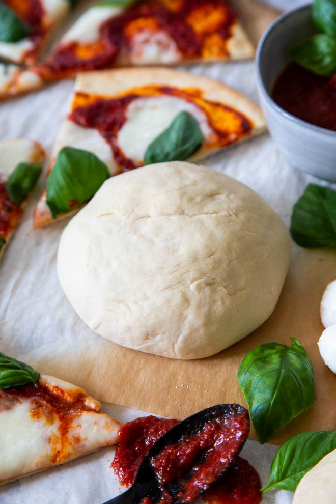 no fuss five minute pizza dough, dough ball surrounded by cut pizza margarita with fresh basil