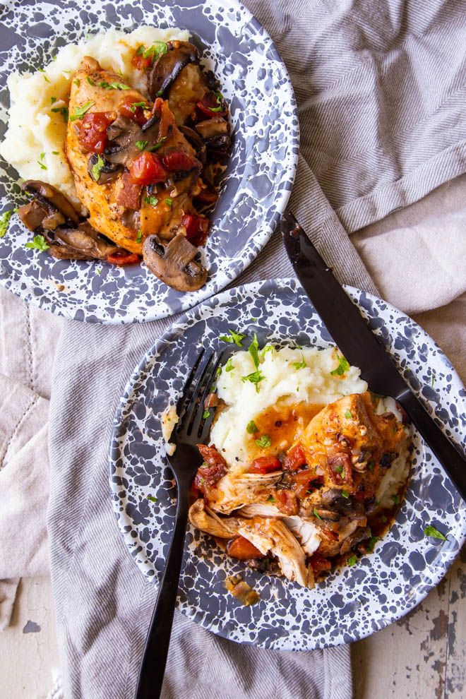 Two dishes of Instant Pot Rustic Braised Chicken set on mashed potatoes in a shallow gray and white bowls shot from overhead on tan napkins