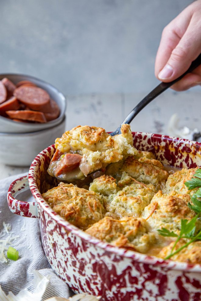 Full on comfort food with andouille sausage and chicken pot pie, topped with cheesy herbed biscuits being lifted from pot with a large black spoon