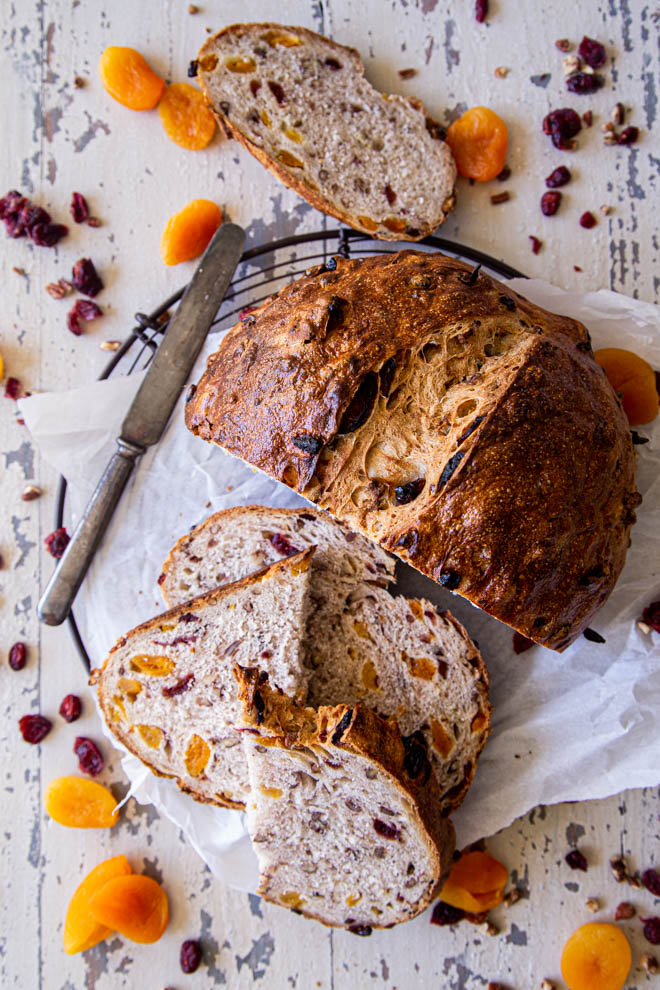 Large round loaf of apricot cranberry pecan bread, sliced and shot overhead with scattered apricots around.