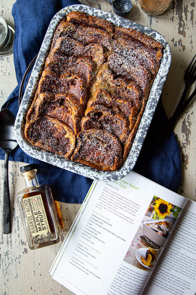 baked french toast in a gray and white speckled dish with open cookbook, shot overhead
