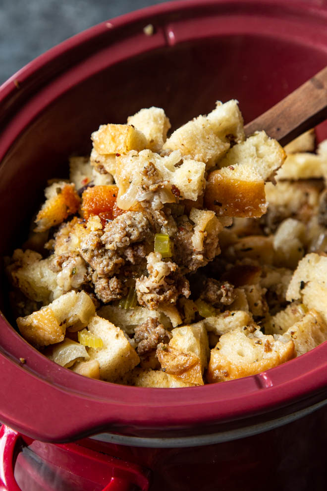 Slow cooker apple sausage stuffing in a red slow cooker on a dark background