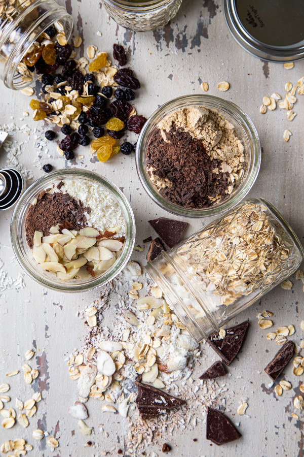 5 mason jars with overnight oats recipes, with chocolate and oats on a white distressed board with a photo overhead