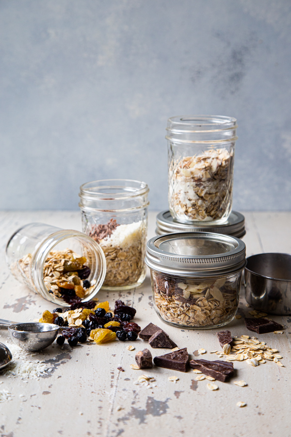 5 mason jars with overnight oats recipes, with chocolate and oats on a white distressed board
