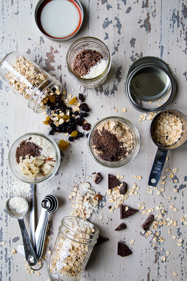 5 mason jars with overnight oats recipes, with chocolate, dried fruit and coconut on a counter
