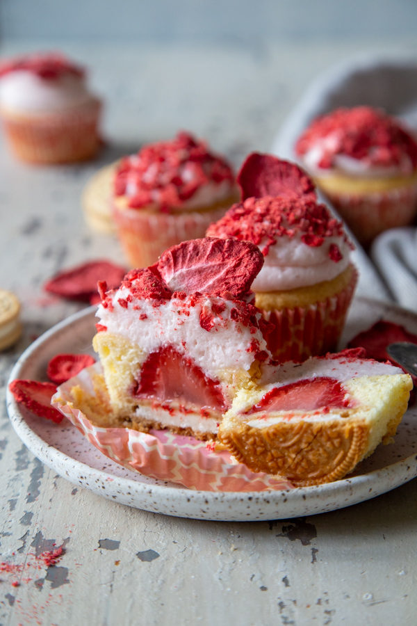 overhead photo of strawberry shortcake cupcakes, cut in half on a white speckled plate