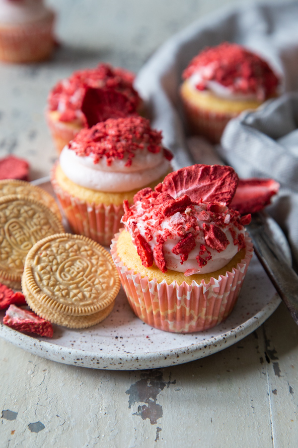 photo of strawberry shortcake cupcakes on a white speckled plate and golden Oreos beside it