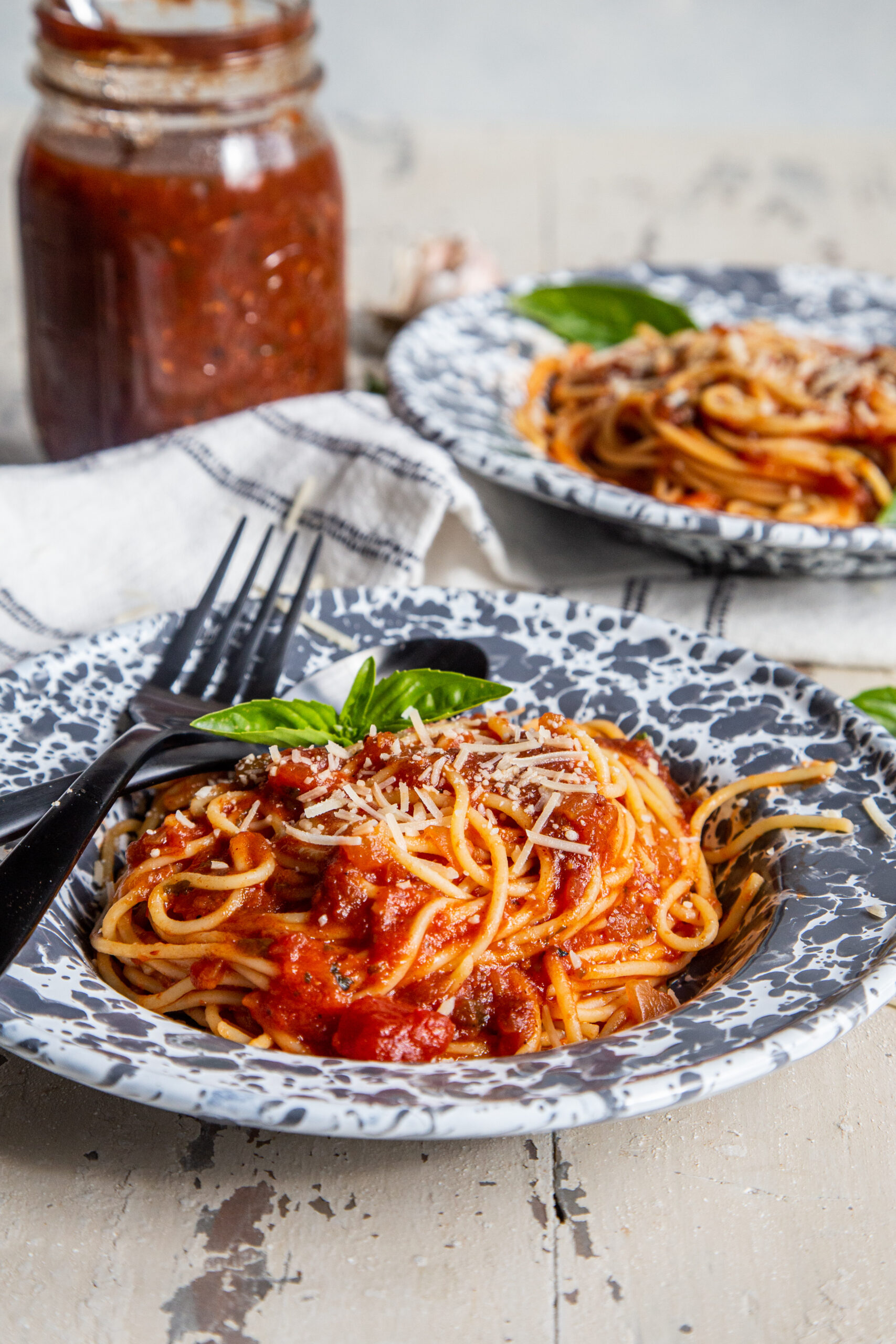 Two bowls of spaghetti topped with pasta sauce, shredded parmesan, and basil
