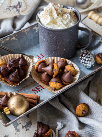 Two muffin wrappers filled with acorn cookies, on tray with hot chocolate mug
