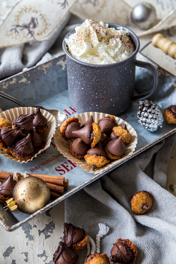 Two muffin wrappers filled with acorn cookies, on tray with hot chocolate mug