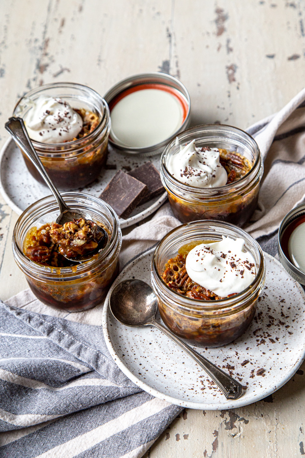 Four mason jars of chocolate pecan pie, with 3 garnished with whipped cream and chocolate shavings