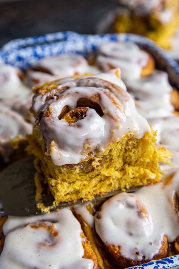 Cinnamon roll being lifted from baking dish