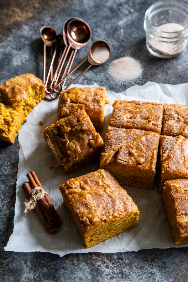 Pumpkin snack cake on parchment paper with cinnamon sticks, measuring spoons, and cinnamon sugar