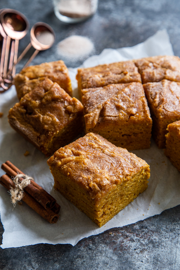Squares of pumpkin snack cake on parchment paper next to bundle of cinnamon sticks