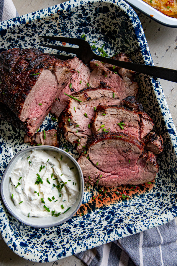 Sliced grilled beef tenderloin with serving fork and bowl of horseradish chive sauce