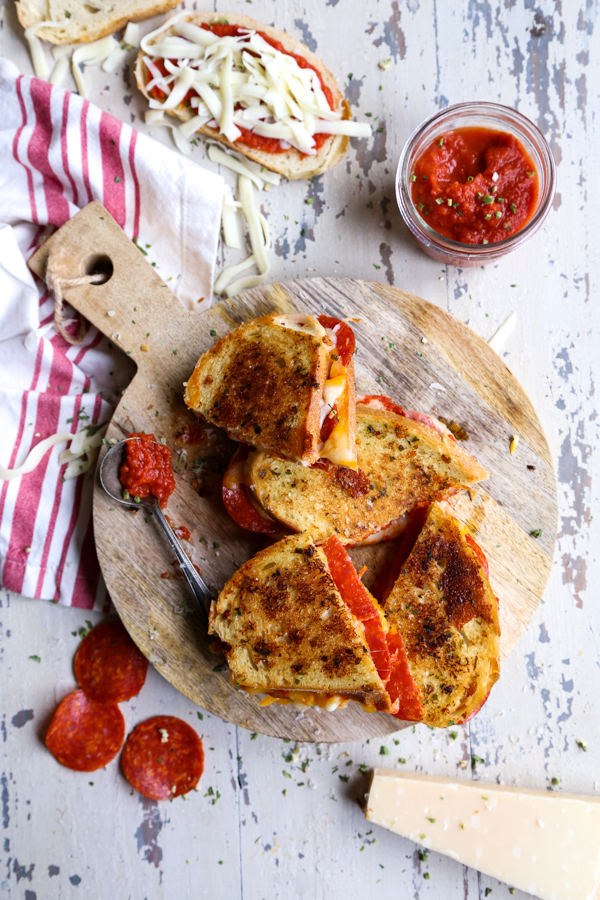 Pepperoni Pizza Grilled Cheese on a wood cutting board with a jar of pizza sauce on the side