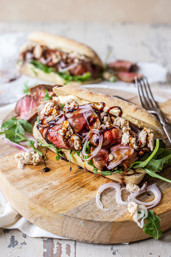 Sirloin steak sandwich on a cutting board with onions and balsamic glaze
