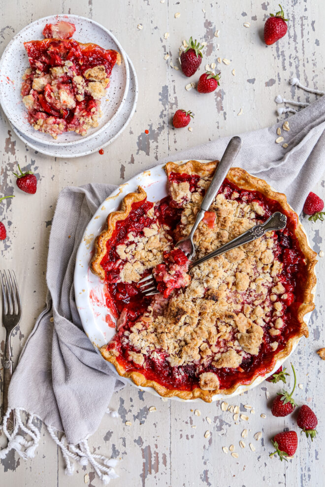 Strawberry crumble pie shot overhead on a white barn backdrop with strawberries around the pie dish