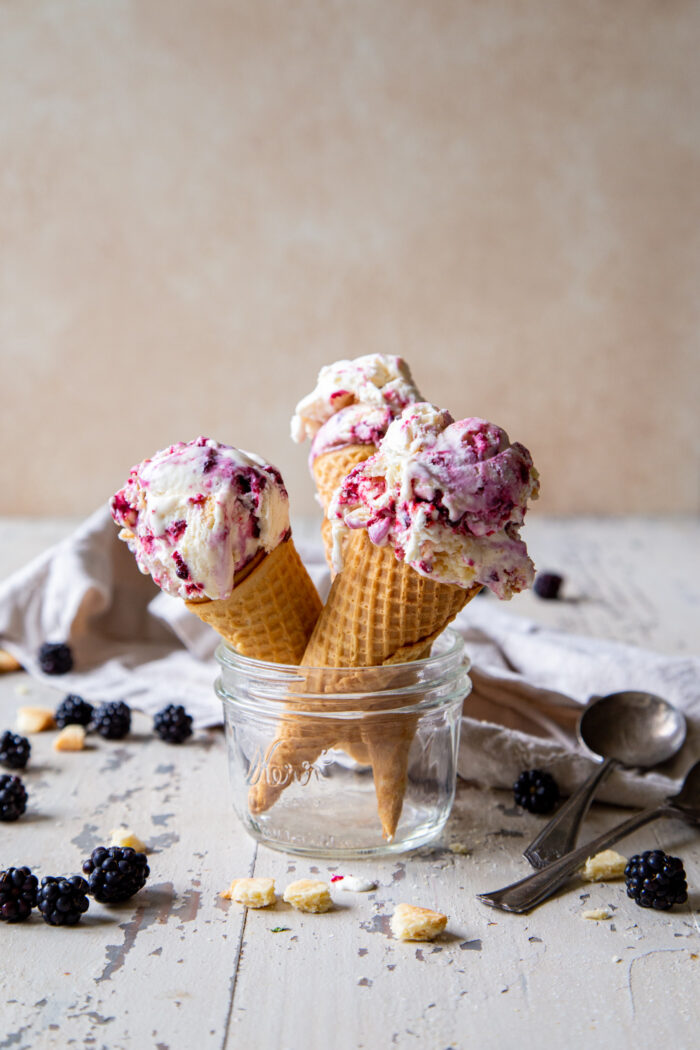 2 cones of blackberry pie no churn ice cream set in a mason jar with fresh blackberries and pie crust scattered around