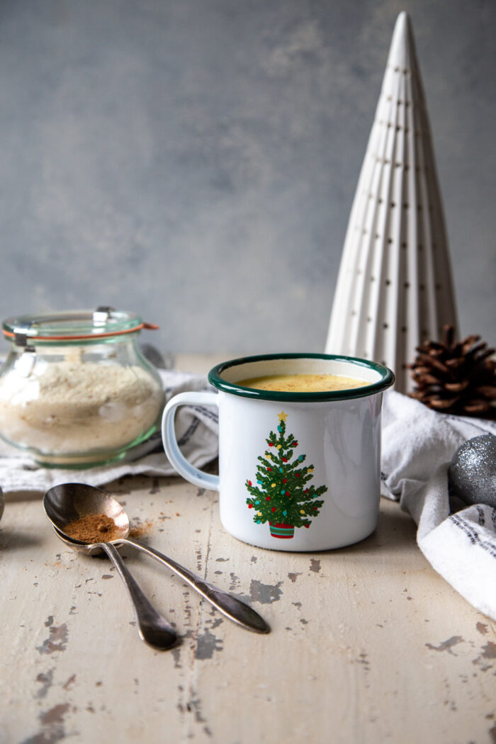 eggnog white chocolate hot cocoa in a white enameled mug with a christmas tree on it