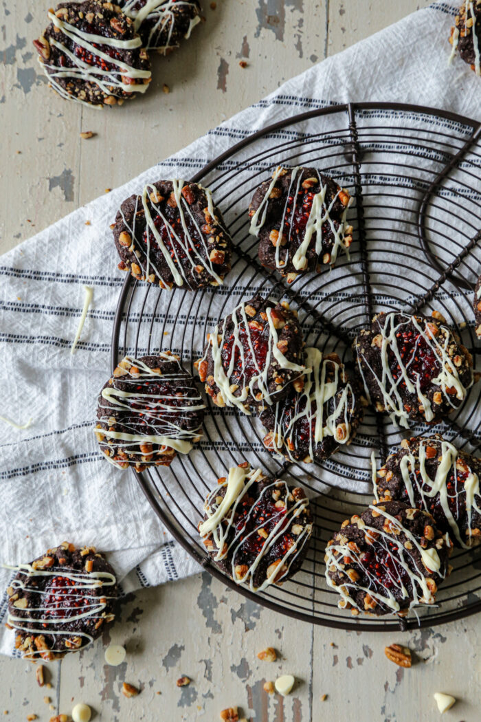 Chocolate raspberry thumbprint cookies on a dark wire baking rack on a white napkin