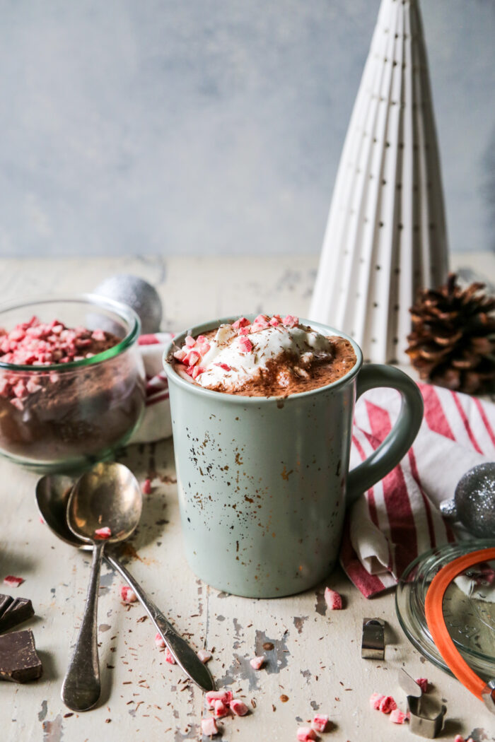 Peppermint Hot Cocoa Mix on a distressed background in a mason jar behind a mug of hot cocoa in a green mug