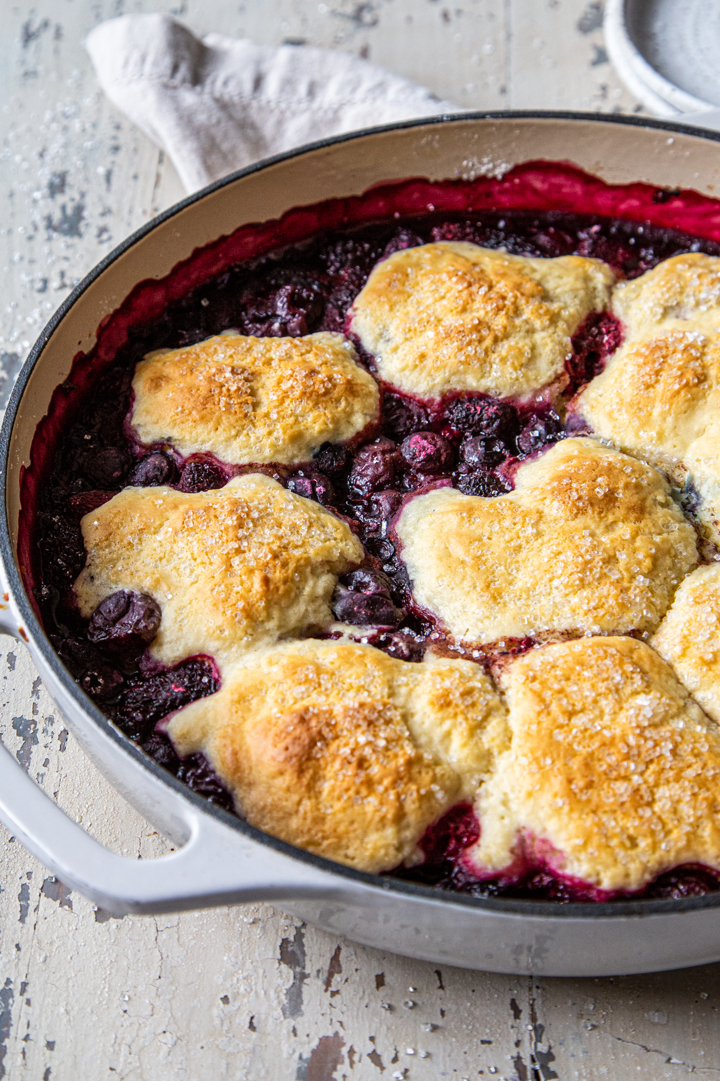 Easy cast iron berry cobbler in white cast iron pan shot close up to see the sparkling sugar on the biscuit topping