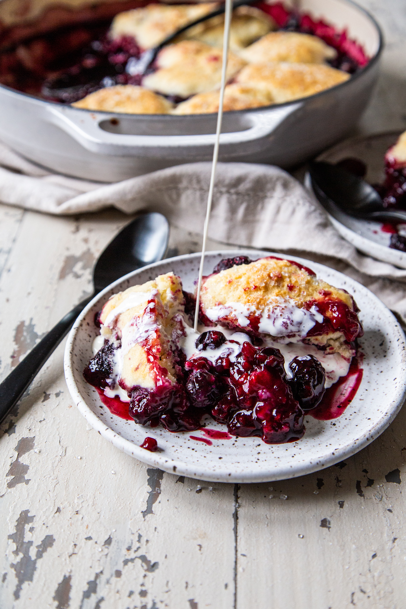 Easy cast iron berry cobbler in white plate with cream poured over the top