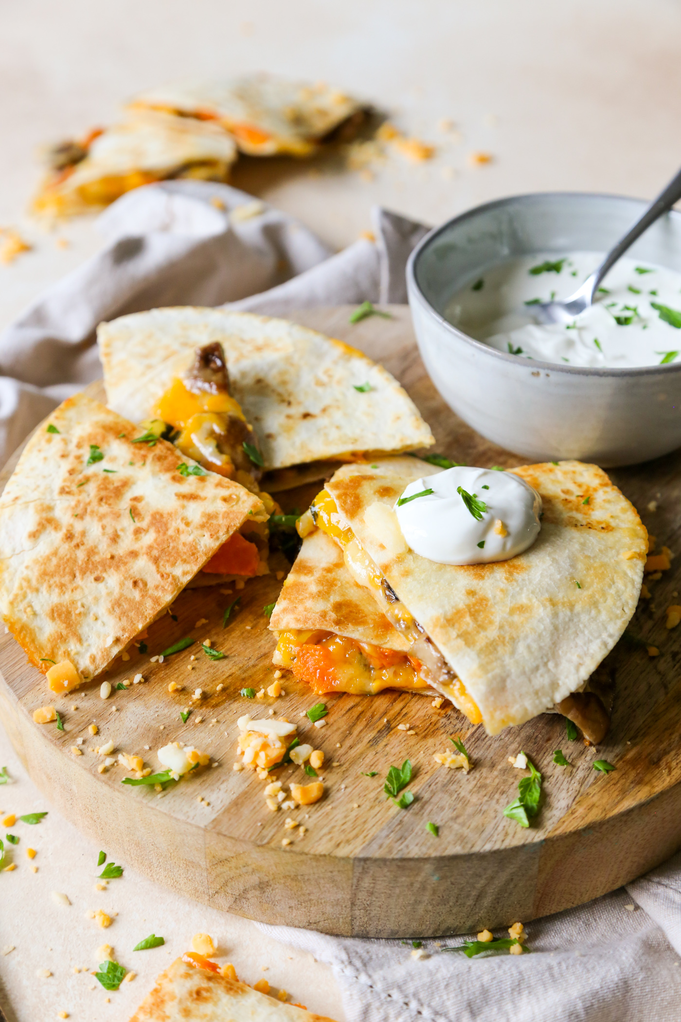 Steak Mushroom and Squash Quesadilla is a luxury leftover dream recipe on a cutting board, with sprinkled cheese, and a dollop of sour cream on top.