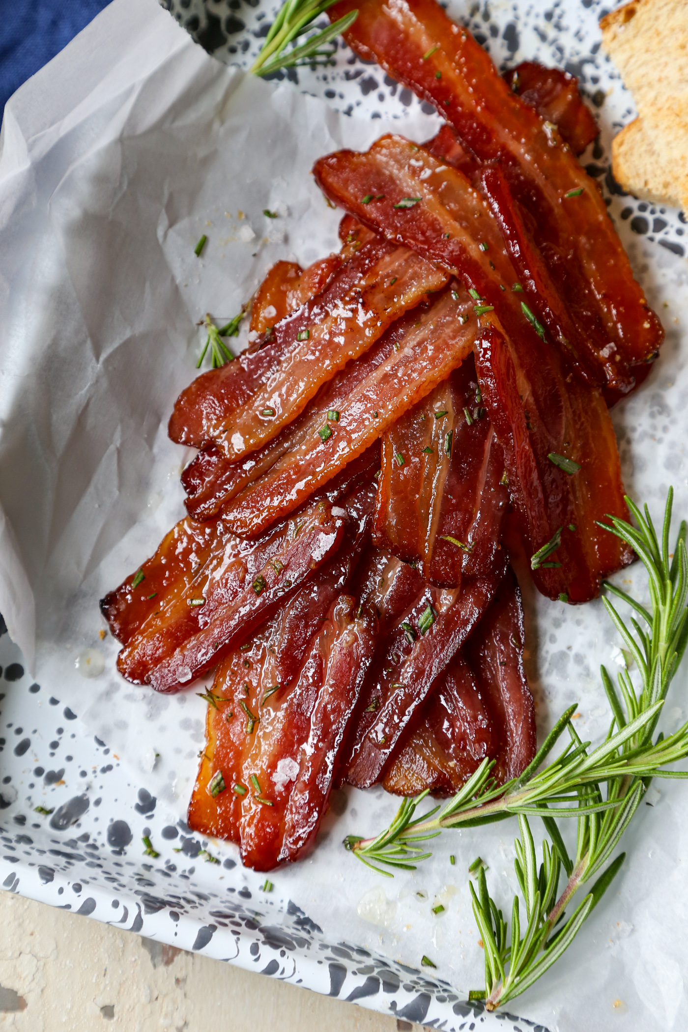 Maple rosemary bacon cooked in the oven on a parchment lined baking sheet with rosemary sprigs and toast