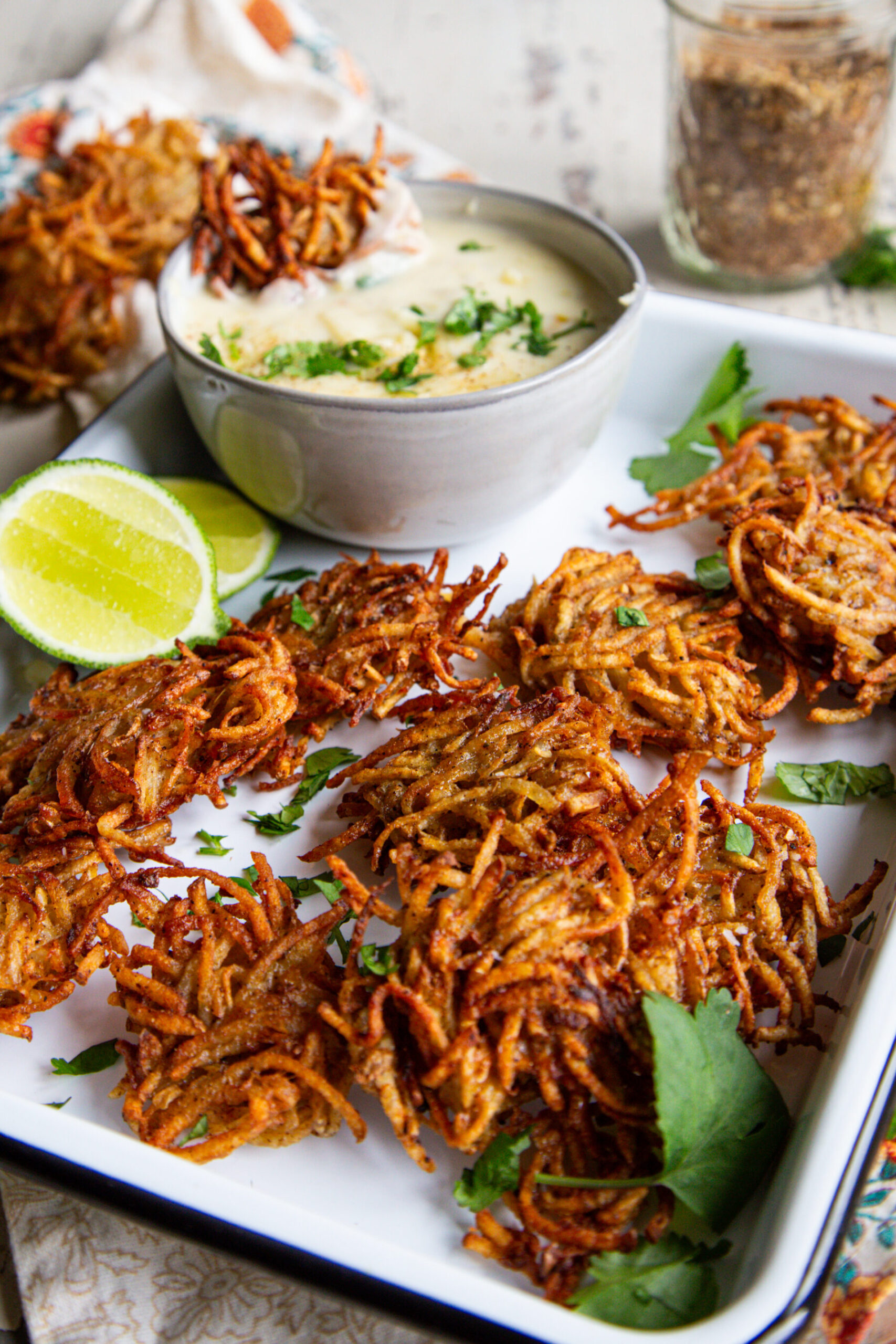 Close up shot of taco spiced potato fritters / latkes on a white baking sheet with a bowl of cheese dip and lime