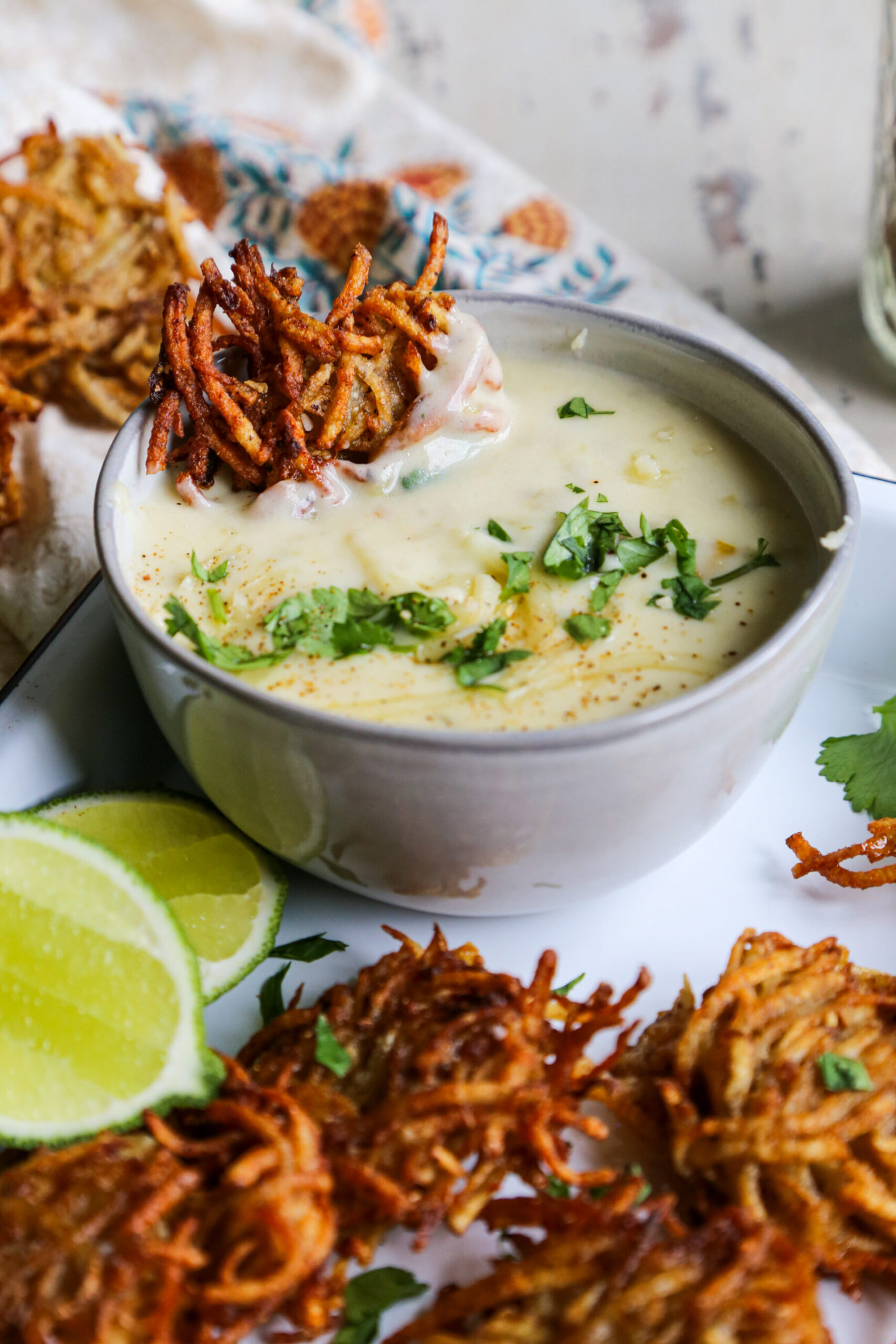 Close up shot of taco spiced potato fritters / latkes in a bowl of white baking sheet with a bowl of cheese dip and lime
